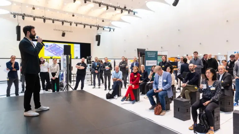 Mann steht auf Bühne. Menschen sitzen vor ihm und hören zu.