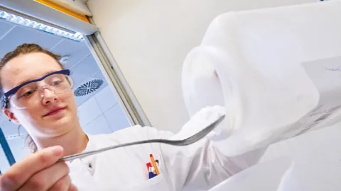Person holt mit einem Löffel aus einer Verpackung AEROSIL heraus