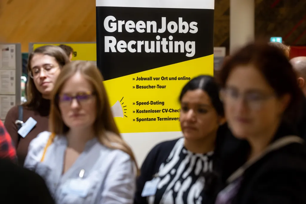 Junge Menschen die einem Vortrag zuhören. Im Hintergrund ein Plakat, auf dem GreenJobs Recruiting steht.